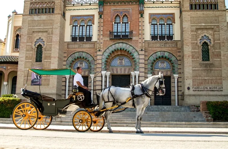 Un coche de caballos tradicional ante el Pabellón Mudéjar de Sevilla