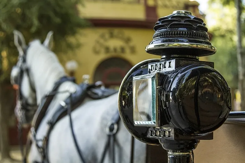 Farol de un carruaje tradicional con un caballo blanco al fondo