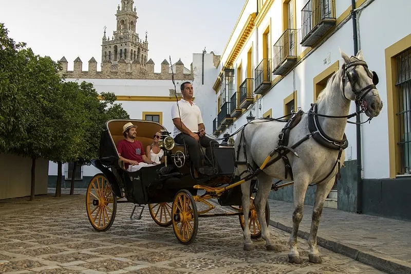 Pasajeros disfrutando de un paseo en coche de caballos por Sevilla